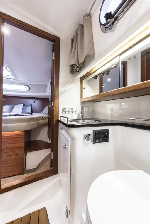 Interior of a yacht bathroom featuring a sink, mirror, shower controls, and a doorway leading to the bedroom.